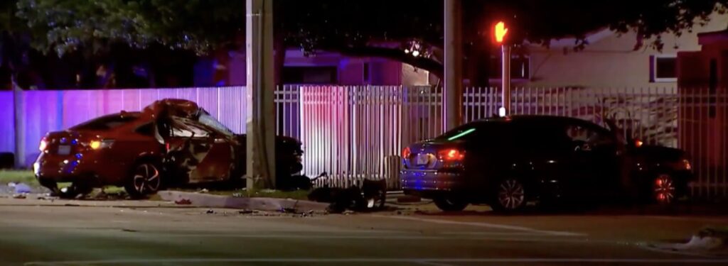 Nighttime image of a car accident scene in Naranja with two damaged vehicles, emergency lights, and a metal fence, showing the severity of the crash.